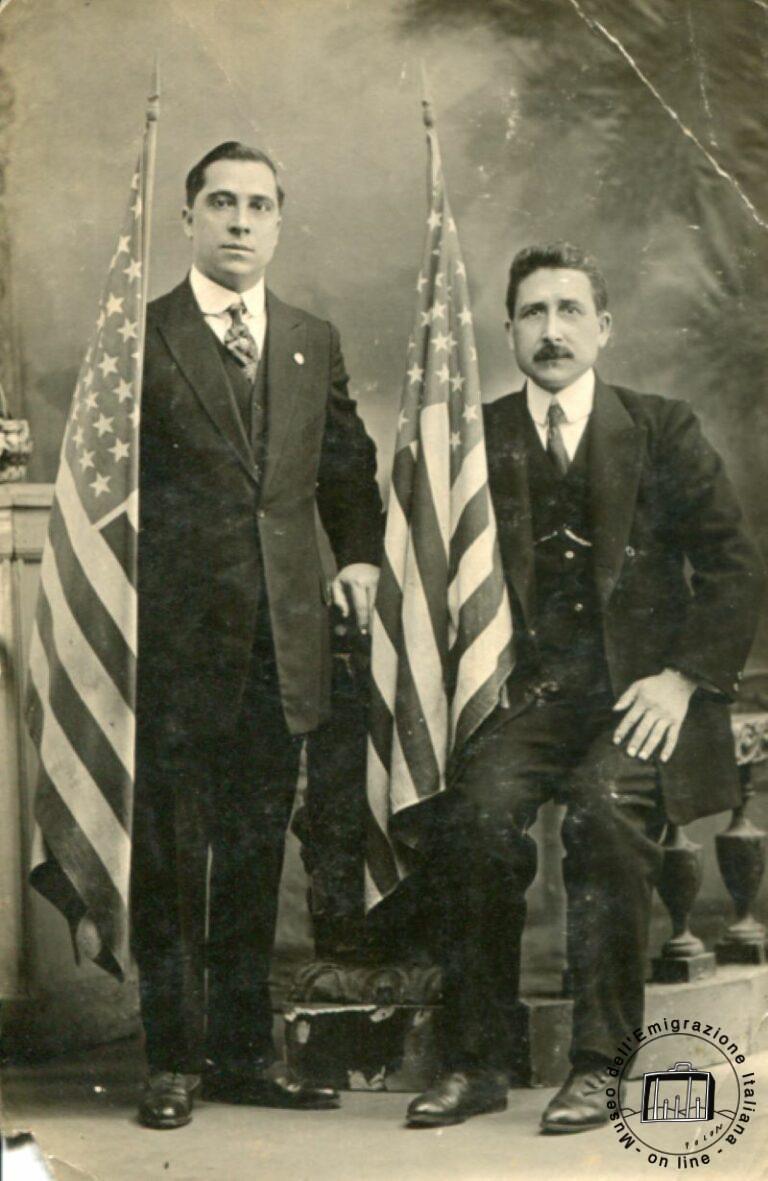 Fidelidad a los Estados Unidos, la nueva patria. Raffaele Ciaccio, sentado, y un amigo estrechan en las manos la bandera americana